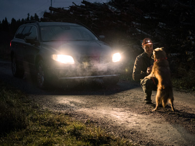 Man with dog in front of a vehicle with the headlines on