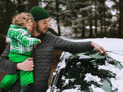 Father holding daughter while scraping off car window.