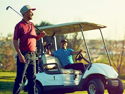 Man standing next to golf cart with a club while another man sitting in drivers seat