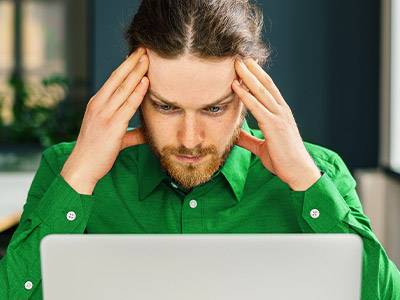 Man wearing green looking upset at his macbook
