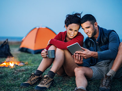 Man and a woman looking at a tablet while camping