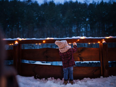 Little girl looking at lights wrapped around a fence